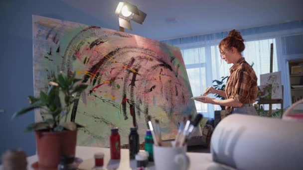 Yetenekli kadın sanatçı enerjik bir şekilde boya fırçası kullanıyor. Kirli elleri boyalı kız stüdyoda sanat eseri yaratıyor. — Stok video