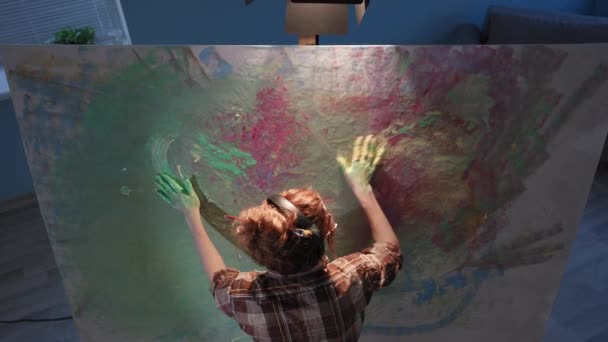 Talentosa artista femenina en auriculares utiliza las manos con pintura, chica con los brazos sucios crea imagen moderna sobre lienzo en el estudio, cámara en movimiento — Vídeos de Stock