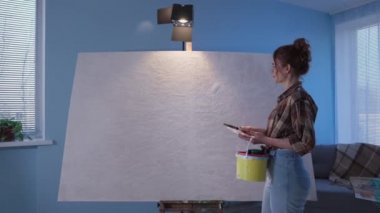 Kız, resim ve fırçalarla dolu bir sehpaya gelir. Gözlüklü kadın ressam sanat sürecinden önce büyük tuvali elleriyle okşar.