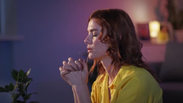 Vrouw gelooft in God bidt met gevouwen handen in liefde op haar knieën in de avond in de kamer voor het slapen gaan, glimlacht en kijkt naar de camera — Stockvideo