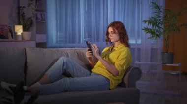 Ev hanımı, akşamları yatmadan önce evdeki kanepede dinlenirken akıllı telefon kullanarak modern teknoloji kullanır ve internetten alışveriş siparişi verir.