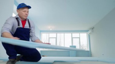 İş üniformalı erkek müteahhit kaplama yapmadan önce polistiren köpükle zemini izole ediyor.