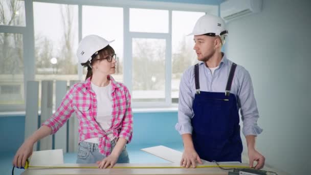 Homem e mulheres em capacetes de construção fazer reparos de piso e corte laminado com ferramenta — Vídeo de Stock