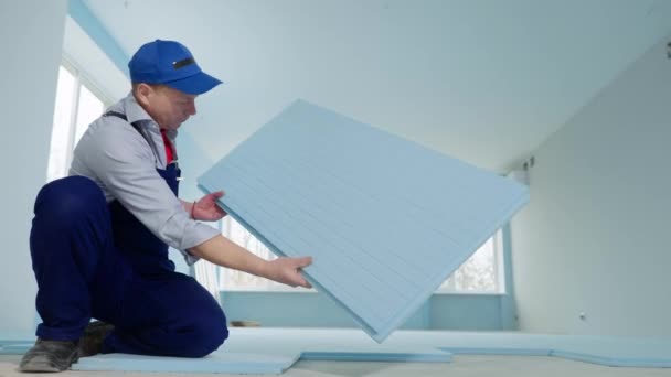 Hombre en uniforme de construcción está colocando aislamiento en el suelo antes de colocar suelo laminado en el interior — Vídeo de stock