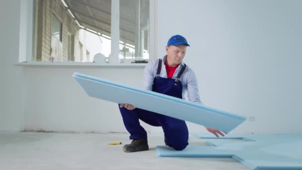 Homem em uniforme realizando trabalhos de construção em ambientes fechados e colocando isolamento de espuma de poliestireno no chão antes de colocar laminado — Vídeo de Stock