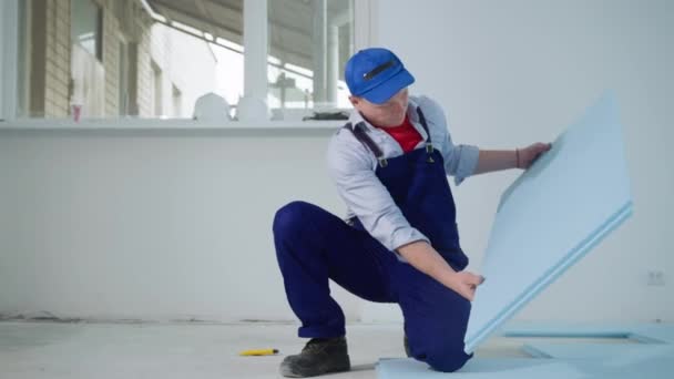 Mężczyzna budowniczy instaluje izolację podłogową w przygotowaniu do podłóg laminowanych — Wideo stockowe