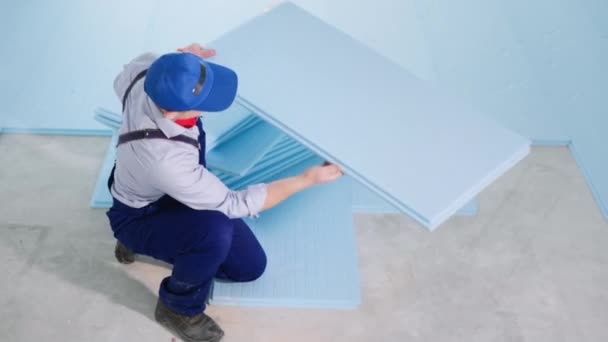 Homem em roupas de trabalho funciona como construtor no local de construção e estabelece espuma de poliestireno expandido para isolamento térmico e colocação de laminado no chão — Vídeo de Stock