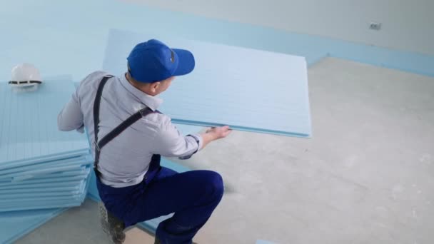 Construtor profissional masculino estabelece material de construção para isolamento de piso antes de colocar piso laminado no local de construção — Vídeo de Stock