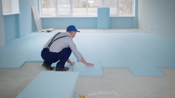 Male construction site worker insulates floor with polystyrene foam to lay laminate indoors — Stock Video