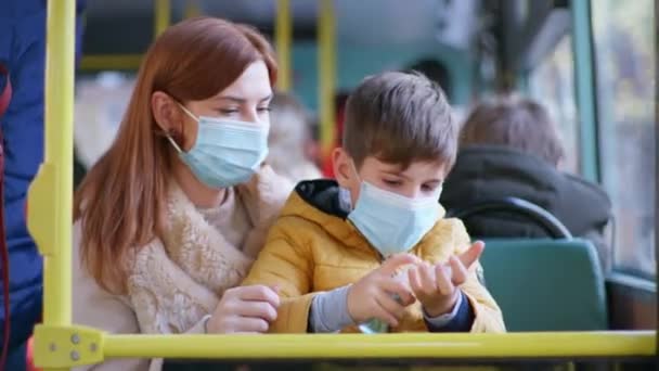 Genitore femmina con figlio in braccio in maschera medica tratta le mani con antisettico a causa di infezione coronavirus durante il viaggio — Video Stock
