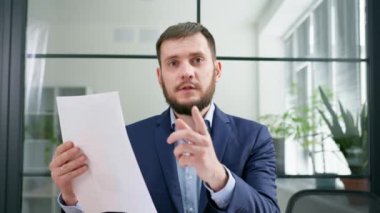 İş adamı bilgisayarında webcam kullanarak konuşuyor, toplantı ve konferans süresince belgeleri tartışıyor, kameraya bakıyor.