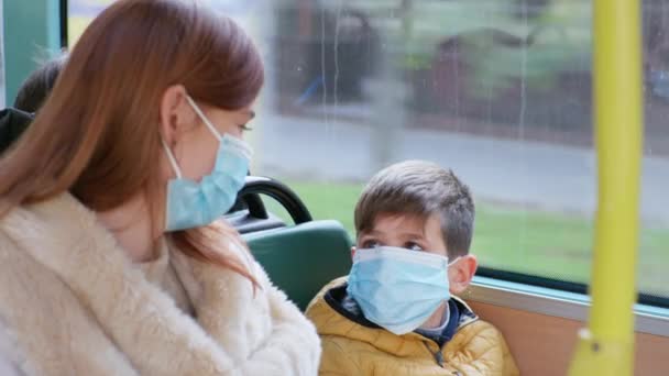Молода жінка з хлопчиком в медичній масці буде вживати запобіжних заходів для захисту від коронавірусної інфекції подорожей на громадському транспорті — стокове відео