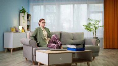 Evrakları ve dizüstü bilgisayarı elinde pijamaları ve pijamalarıyla genç ve çekici bir ofis çalışanı odasındaki kanepede çalışıyor.