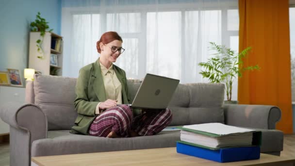 Funcionária feminina vestindo blazer e calças de pijama realiza uma conferência online usando webcam no laptop enquanto trabalha em quarentena em casa — Vídeo de Stock