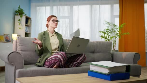 ジャケットとパジャマパンツの女性は自宅で隔離中にノートパソコンのビデオリンクでオンラインで交渉しています — ストック動画