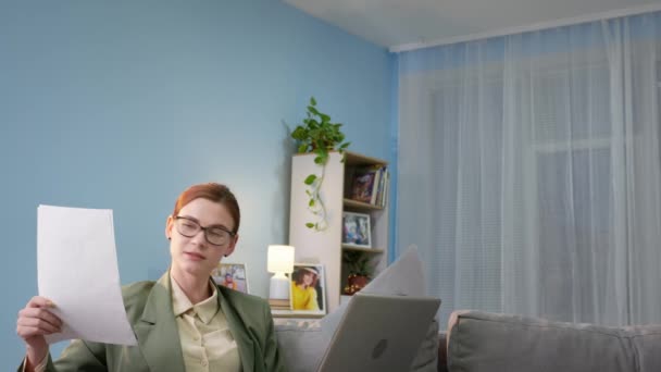 戴眼镜的女人穿夹克和睡衣的女人使用现代技术和应用在电脑上与顾客交谈通过视频链接背景耳机里的男人用真空打扫房间 — 图库视频影像