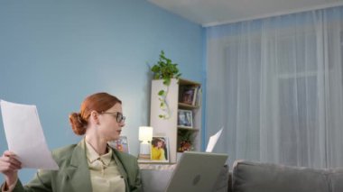 Gözlüklü bir iş kadını, evde internet üzerinden çalışır ve bilgisayarından video iletişimi ile iletişim kurarken kulaklık takan bir adamla ve elinde elektrikli süpürgeyle evi temizler.