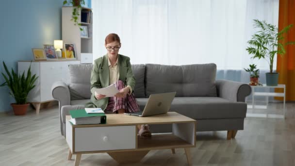 Kobieta nosząca okulary do widzenia kurtki i piżamy rozmawiająca przy użyciu technologii cyfrowych poprzez komunikację wideo na laptopie podczas pracy biurowej w domu — Wideo stockowe