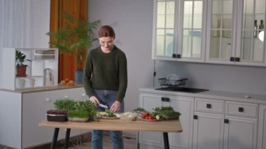 Salata pişirmek, gözlüklü bir kız mutfak masasında mikro yeşilliklerle dururken bıçaklı yeşil bir salatalık kesiyor.