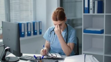 Çok çalışan kadın doktor ofis işi sırasında gözlük takıyor, monitörün önündeki genç kadın hastanede kağıda not alıyor.