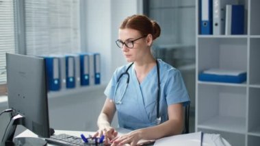Bilgisayarda çalışan yorgun kadın doktor masasında oturan gözlüklerini çıkarırken steteskoplu genç kadın hastanede baş ağrısı çekiyor.