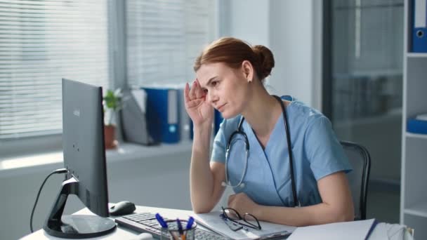 Migräne bei der Arbeit, erschöpfte junge Frau in Uniform massiert gereizte Augen und setzt dann eine Brille auf, um im Krankenhaus am Computer zu arbeiten — Stockvideo