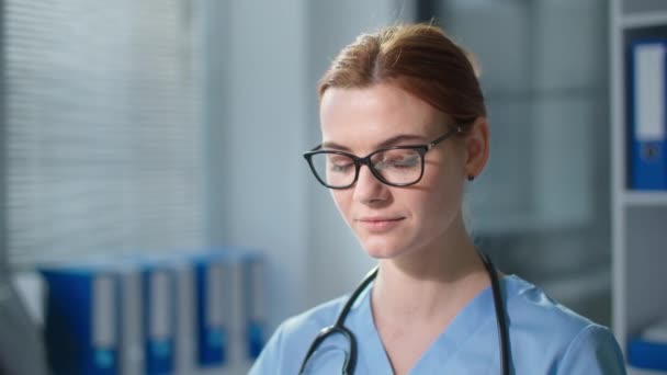 Orvos szemüveg, miközben dolgozik a kórházban, portré boldog női terapeuta gépelés egy számítógép billentyűzetén, majd nézi a kamera mosollyal — Stock videók