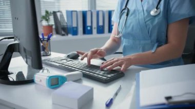 Doktor elleri klavyede daktilo çekiyor, kadın doktor hastane ofisindeki bilgisayarın başında çalışıyor.
