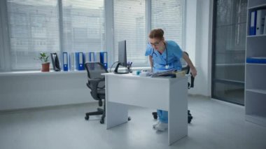 Kadın doktor iş yerinde oturur ve belinde keskin bir ağrı hisseder. Genç kadın rahatlamaya ve elleriyle acıyı hafifletmeye çalışır.