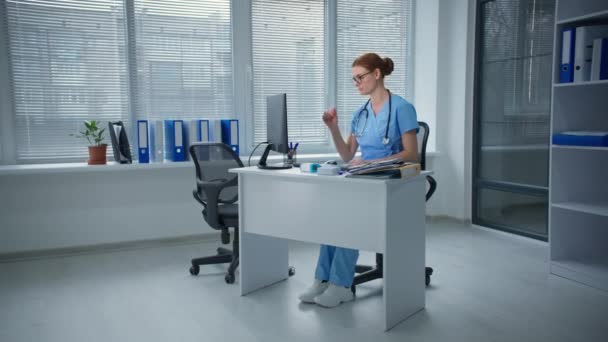 仕事中の片頭痛医者は頭痛を感じ病院のテーブルに座りながら眼鏡をはずします — ストック動画