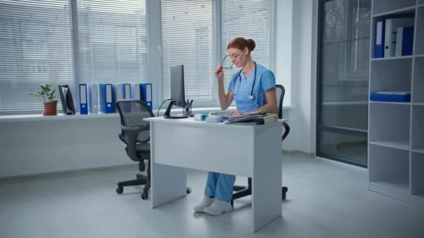 不幸なことにストレスを感じる女性医師圧力と強い頭痛病院に座っている痛み,動揺病気の医師は、コンピュータの近くに彼の眼鏡を脱いで頭に触れます — ストック動画