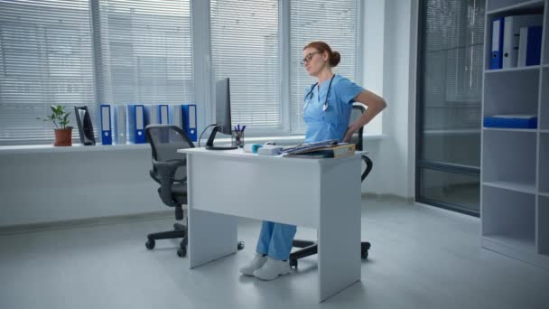 バックキャッシュブルーの制服を着た女性医師が突然パソコンの病院に座って腰を痛めて — ストック動画
