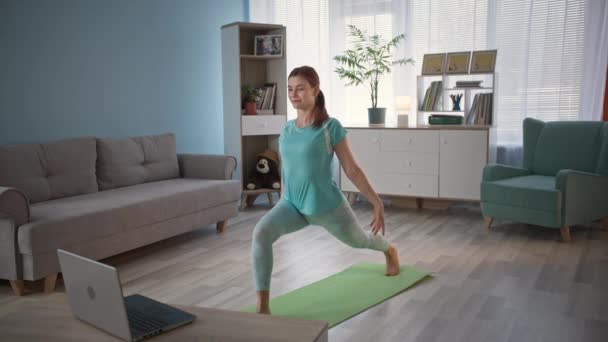 Jovem mulher em traje realiza exercícios físicos no tapete de ioga com professor de ioga via link de vídeo, estilo de vida — Vídeo de Stock