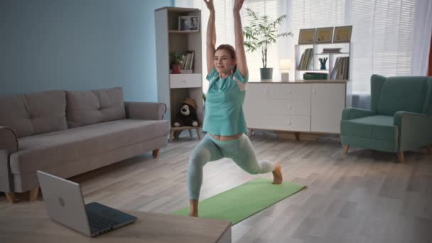 Menina encantadora em uniforme esportivo realiza exercícios físicos usando vídeo ocupado no laptop — Vídeo de Stock