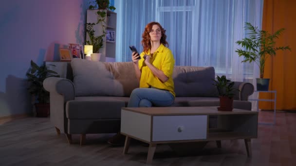 Háziasszony visel szemüveg használ mobiltelefon, miközben ül a kanapén, miközben pihennek a nappaliban éjjel — Stock videók