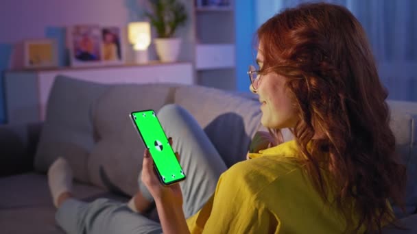 Nő egy okostelefon a kezében néz egy zöld képernyőn, miközben pihenni az ágyon a szobában otthon, — Stock videók