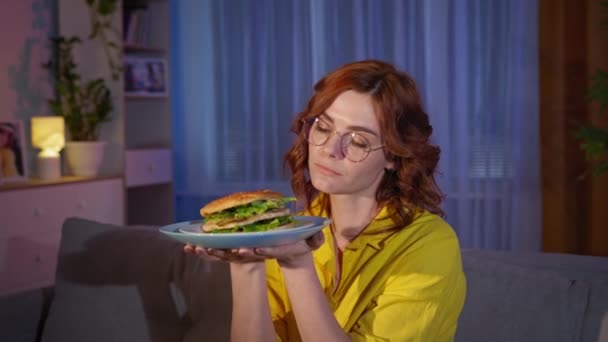 Głodna kobieta z hamburgerem w rękach jest na diecie i odmawia jedzenia fast foodów, — Wideo stockowe