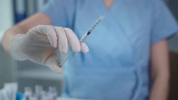 Lékař v modré uniformě a ochranných rukavicích drží injekční stříkačku s vakcínou v ruce, tekutina protéká jehlou zblízka — Stock video