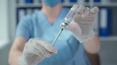 İğne cam şişenin plastik mührünü patlatıyor ve ilaç kazanıyor. Koruyucu eldivenlerdeki tıbbi eller yakın plan Coronavirus aşısını tutuyor.