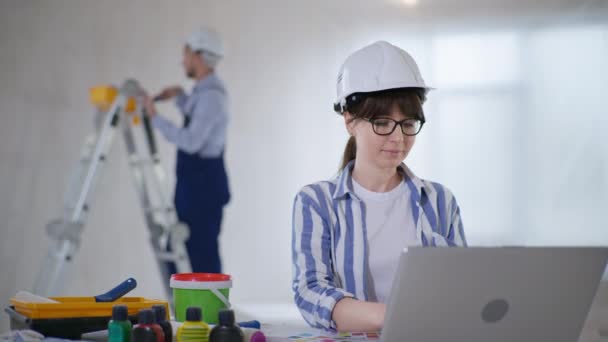 Perempuan dalam helm dengan kacamata untuk pekerjaan penglihatan di notebook dan memilih latar belakang wallpaper baru pembangun laki-laki dinding lukisan — Stok Video