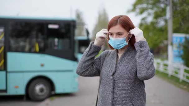 Young woman puts on a medical mask to protect against virus and infection for a city bus ride — стоковое видео