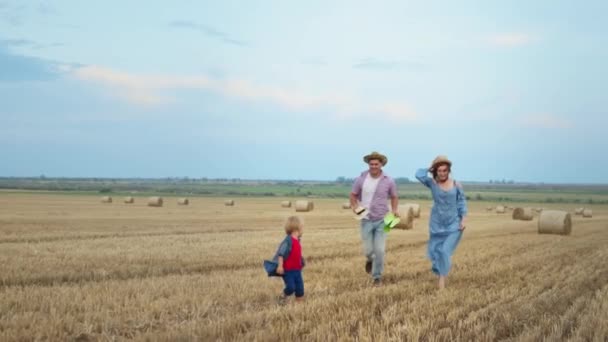 両親は子供を追いかけて田舎の外出中に頭に藁帽子をかぶり — ストック動画