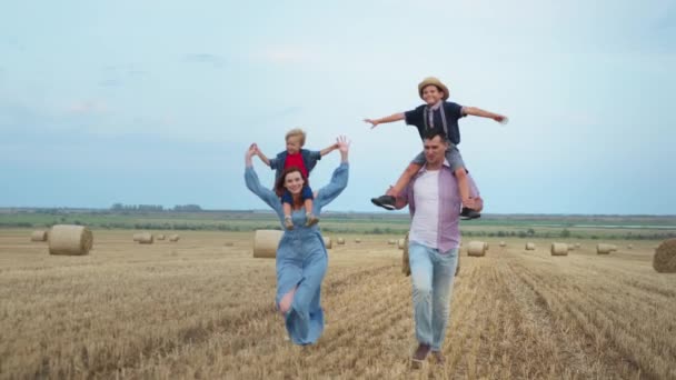 Братья сидят на плечах своих родителей на пшеничном поле — стоковое видео