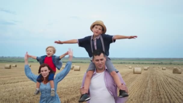 Мужчина и женщина веселятся, бегая со своими сыновьями на шеях своих родителей — стоковое видео