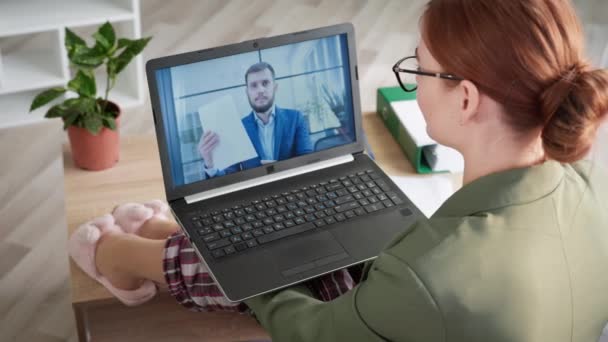 Mujer joven en pijama hablando con el ejecutivo masculino en el chat de vídeo remoto en la pantalla del ordenador mientras está sentado en el sofá en la oficina en casa durante la cuarentena — Vídeos de Stock