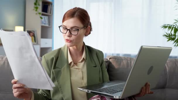 Kobieta freelance pracuje w biurze zdalnie i komunikuje się z klientem za pośrednictwem komunikacji wideo na laptopie podczas siedzenia w domu ana kanapie — Wideo stockowe