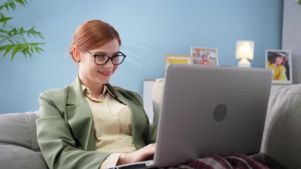 穿着睡衣裤的女商人坐在沙发上，在家里用笔记本电脑远程办公 — 图库视频影像