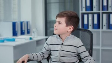 happy boy, portrait of little patient sitting in a chair in the hospital office against the background of many folders