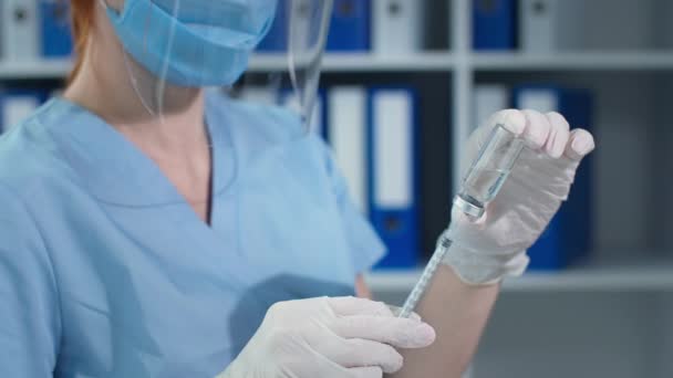 Cuidado de la salud, médico enmascarado en uniforme azul y guantes protectores con jeringa perfora el sello de goma de la ampolla de vidrio y recibe el medicamento — Vídeo de stock