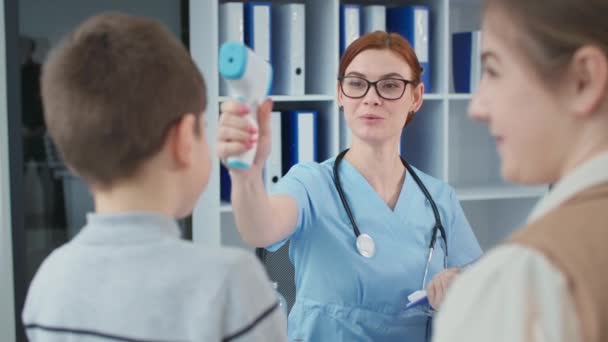 Health care, pediatrician with stethoscope writes notes on a clipboard and measures little patient temperature with a non-contact thermometer in hospital office — Stock video